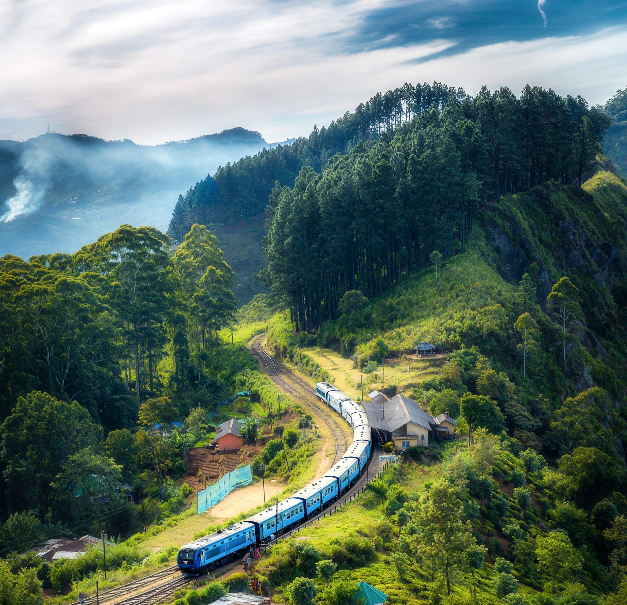Aerial view of a picturesque train winding through lush green hills and rural houses.